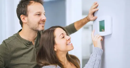 Couple adjusting a smart thermostat on a wall